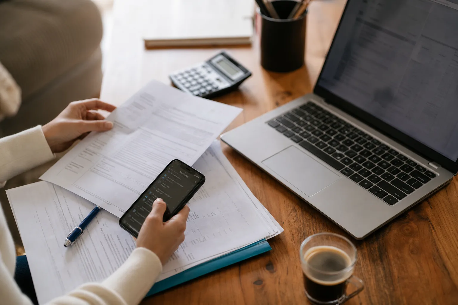 Personne consultant une application bancaire sur smartphone à côté de documents de déclaration fiscale