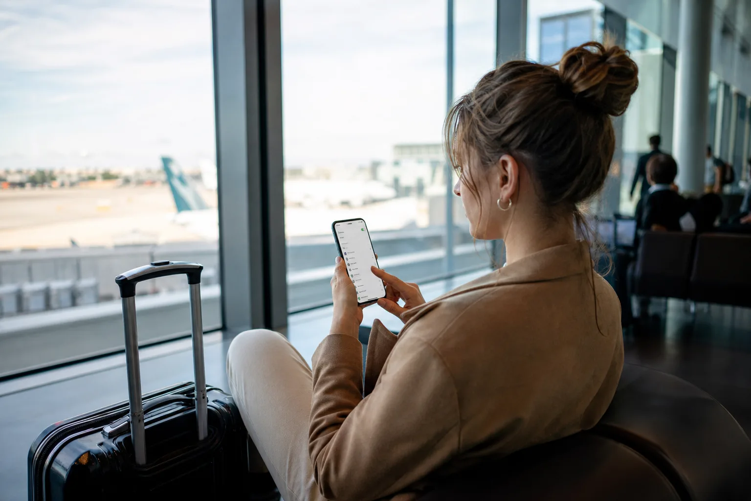 Voyageur consultant son smartphone à un comptoir d'aéroport, écran affichant un réglage de carte SIM virtuelle, ambiance terminal international