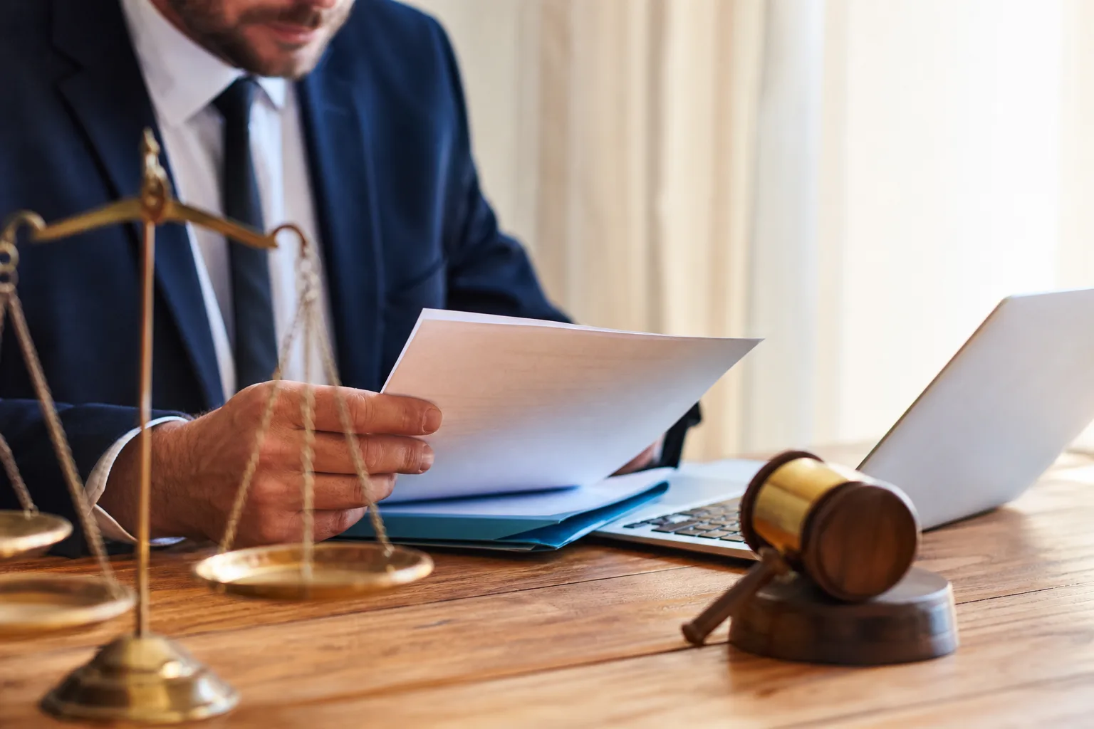 Un avocat en costume examine un document juridique à son bureau, avec une balance de la justice et un marteau de juge au premier plan